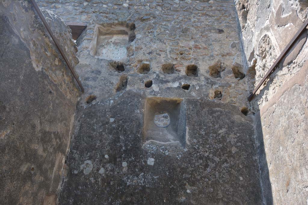 IX.5.2 Pompeii. May 2017. Room ‘q’, looking towards upper west wall and upper floor, with rectangular niche.
Foto Christian Beck, ERC Grant 681269 DÉCOR.
According to Boyce –
in the west wall of a room on the upper floor, above the first room on the west side of the peristyle, was a rectangular niche (h.0.60, w.0.50, d.0.28). 
On its back wall was painted the figure of Vesta (or Epona?), seated upon an ass (or with an ass nearby).
The account in the Not. Scavi describes the two serpents at an altar painted below the niche, though they are not mentioned by either Sogliano or Mau.
The layer of stucco upon which the figure of Vesta was painted has fallen away, partially revealing beneath it an earlier layer, upon which can still be seen two standing figures, each wearing a green garment and having a large yellow bulla suspended from his neck; they are both alike and their posture suggest that of the Lares. 
See Boyce G. K., 1937. Corpus of the Lararia of Pompeii. Rome: MAAR 14. (p. 85, no. 420). 
See Giacobello, F., 2008. Larari Pompeiani: Iconografia e culto dei Lari in ambito domestico. Milano: LED Edizioni, (p.206, no.100).


