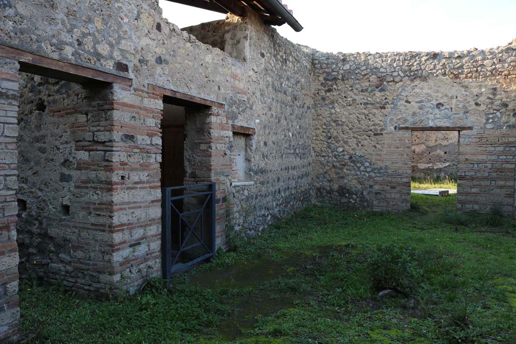 IX.5.16 Pompeii. December 2018. 
Looking north across atrium a’ from entrance doorway, on right is the doorway into the atrium “b” of IX.5.14.
On the left (west) side of atrium a’, on the left, is the doorway to kitchen and latrine e’.
Centre left, is the doorway to cubiculum f’.  Photo courtesy of Aude Durand.
According to Boyce, on the south wall of the kitchen was a large rectangular panel (h.1.0 w.2.0) of white stucco.
On it were painted two yellow serpents with red crest and beards. 
These were on either side of a tile embedded and projecting from the wall.
A fire was painted on the wall above the tile.
The background was painted with plants, and across the top were two painted garlands.
On each of the garlands was a painted bird.
See Boyce, G. K., 1937. Corpus of the Lararia of Pompeii. Rome: MAAR 14.  (p. 86, no. 425)
See Giacobello, F., 2008. Larari Pompeiani: Iconografia e culto dei Lari in ambito domestico. Milano: LED Edizioni, (p.208, no.102)

