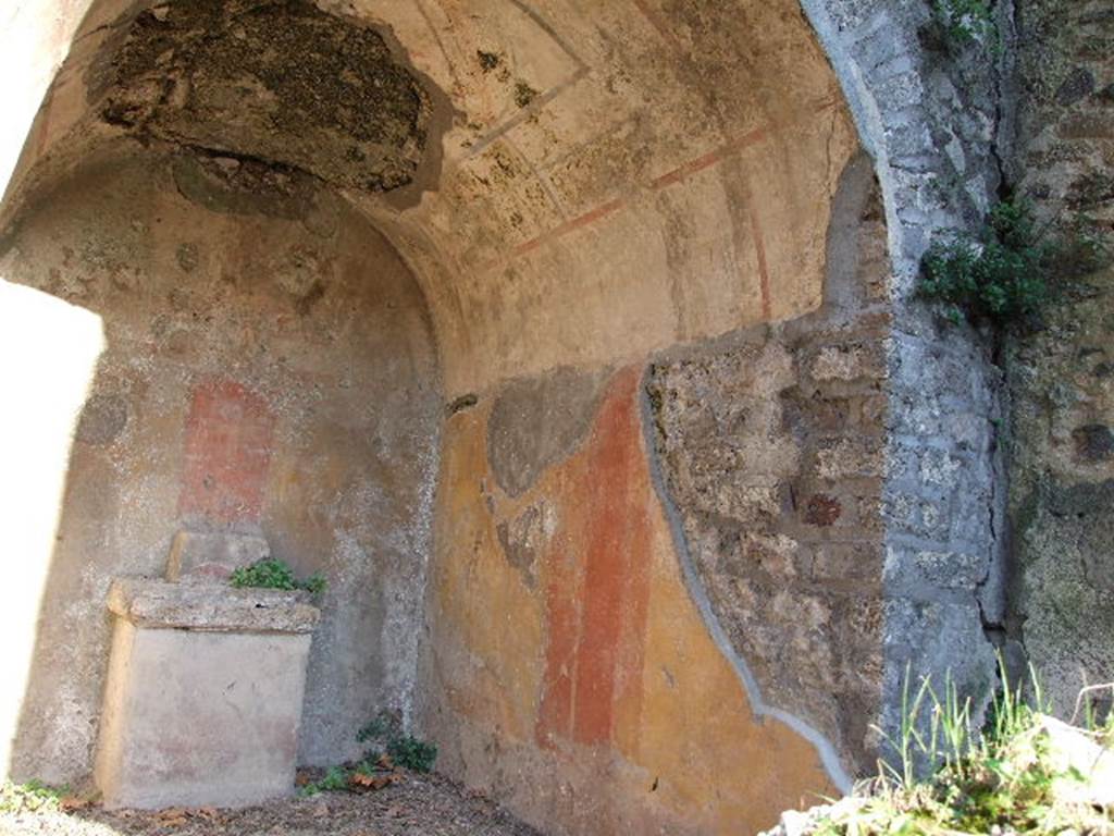 HGE12 Pompeii. December 2006. Lararium with altar, south and east wall. According to Boyce, in an open court was a sacrarium, apparently dedicated to Hercules and Bacchus. Upon the yellow background of the rear wall of a deep niche were painted the attributes of Hercules – a large skyphos and a club. In the pediment on the wall above the niche was painted the figure of Bacchus, accompanied by two flying cupids holding a wreath, one on each side of him. See Boyce G. K., 1937. Corpus of the Lararia of Pompeii. Rome: MAAR 14.  (p.97, no.479)
