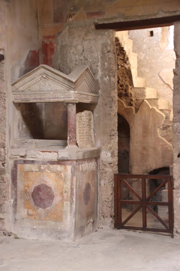 I.10.4 Pompeii. September 2021. 
Looking towards north-west corner of atrium, the lararium and doorway to room 2. 
Photo courtesy of Klaus Heese.
According to Boyce –
A masonry podium (1.08 square, h.1.35) is built into the corner, and above it rises a little temple, formed by a single column at the one free corner of the podium, supporting a roof of two pediments. ………..
See Boyce G. K., 1937. Corpus of the Lararia of Pompeii. Rome: MAAR 14. (p.27-28, no.48).

