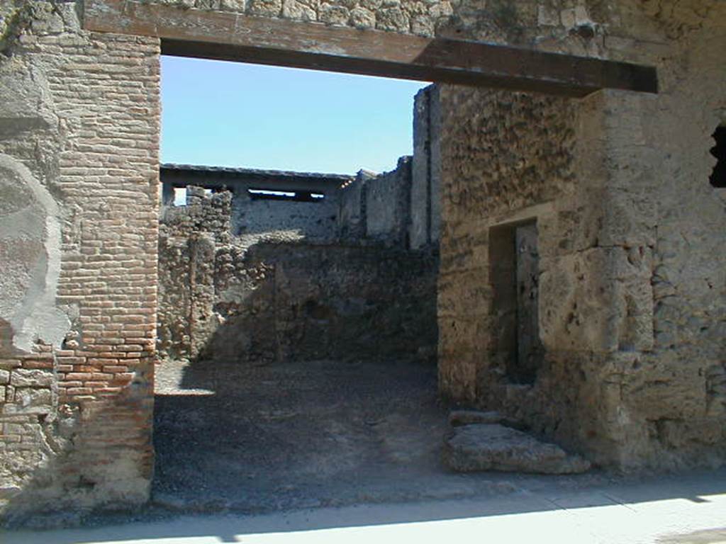 I.7.4 Pompeii. May 2005. Entrance on Via dellAbbondanza. According to Maiuri, the workshop comprised of a large room on the ground floor, and a smaller room in the north-west corner. This smaller room had a small window in its north wall, onto the roadway, as well as a larger window in its east wall overlooking the vestibule of the workshop. 
Against the west perimeter wall was a masonry kitchen area. Found between the kitchen and the rear wall was the recognisable threshold step and traces in the plaster work of a long and steep wooden stairway that would have led up to the upper floor of the room, and from this led both to the balcony and to the other rooms on the upper floor which covered all the space on the ground floor, where there is no trace of an impluvium or possibility of water drainage. Therefore, the roof would have been totally closed and probably only one layer facing the roadway.  The walls of the ground floor were simply plastered with a clear yellow background with simple red lines forming squares.
See Maiuri, A., 1928. Nuovi Scavi nella Via dellAbbondanza. Milano: Hoepli. (p.15-16).
