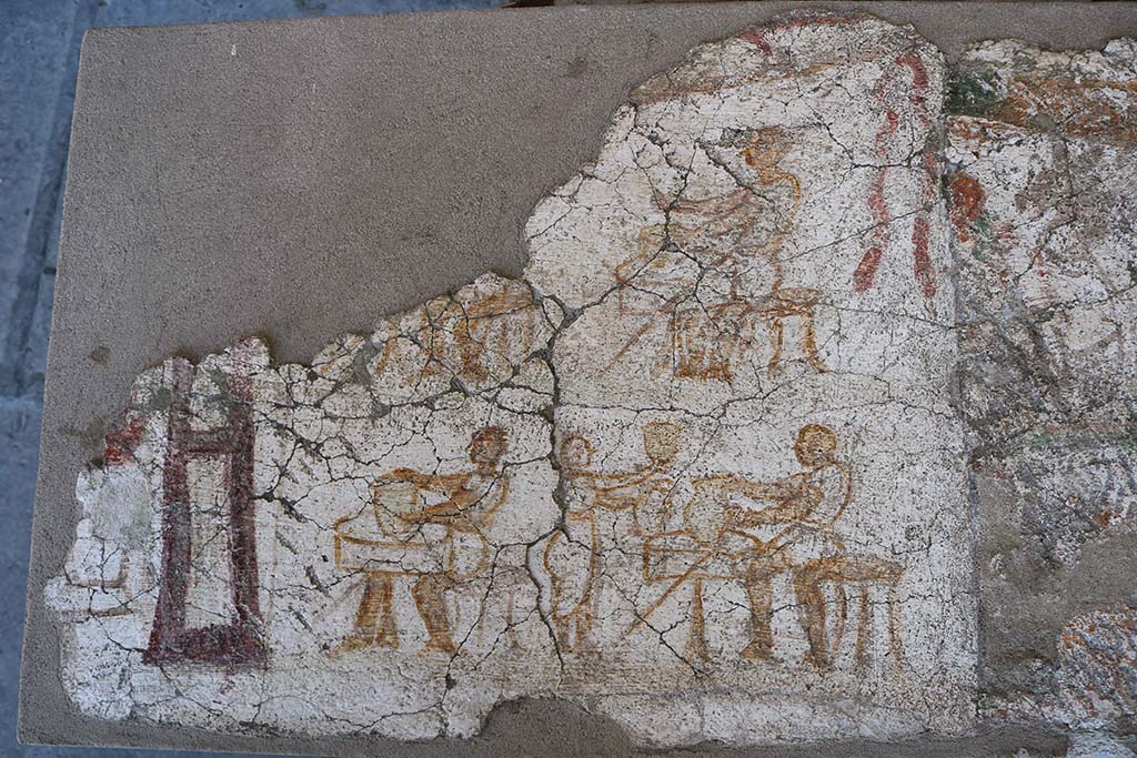 I.8.10 Pompeii. December 2018. Entrance façade painting. 
This shows men seated at tables on which are a variety of vases, possibly indicating a taberna vasaria selling vases.
PAP inventory number 45622.
According to Fröhlich, 
On the left edge, preserved only in the lower part, stands a female deity in long, belted robe with purple edges, probably Minerva. On her right is a round altar covered with burning sacrifices.
The four men are probably potters shaping vessels on one-legged wheels.
Lower right a female customer is examining two vases. Upper right are the remains of a garland.
See Fröhlich, T., 1991. Lararien und Fassadenbilder in den Vesuvstädten. Mainz: von Zabern. (F5, p.307).
