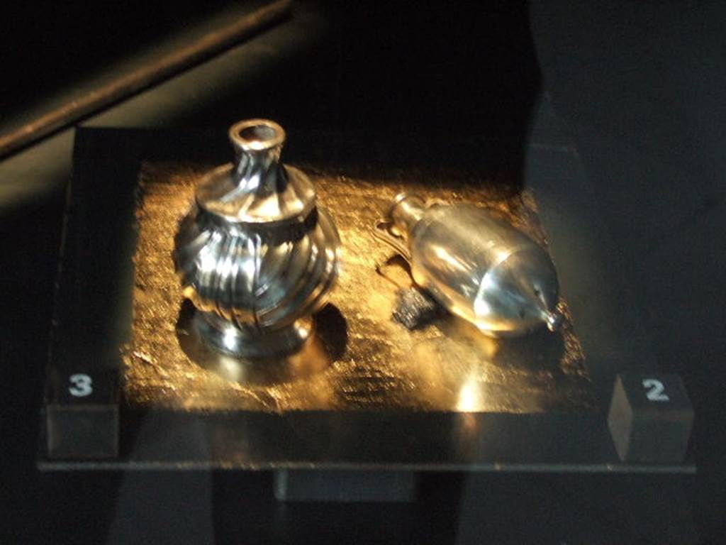 I.10.4 Pompeii. Silver pepper pots. One has the shape of a small amphora. The other has the shape of an aryballos (a small spherical flask). Part of the 115 pieces of Silver found in a chest in the underground storerooms. Now in Naples Archaeological Museum. Inventory numbers 145556 (right) and 145557 (left). See Guzzo, P. (A cura di), 2006. Argenti a Pompei. Milano, Electa. p.222.