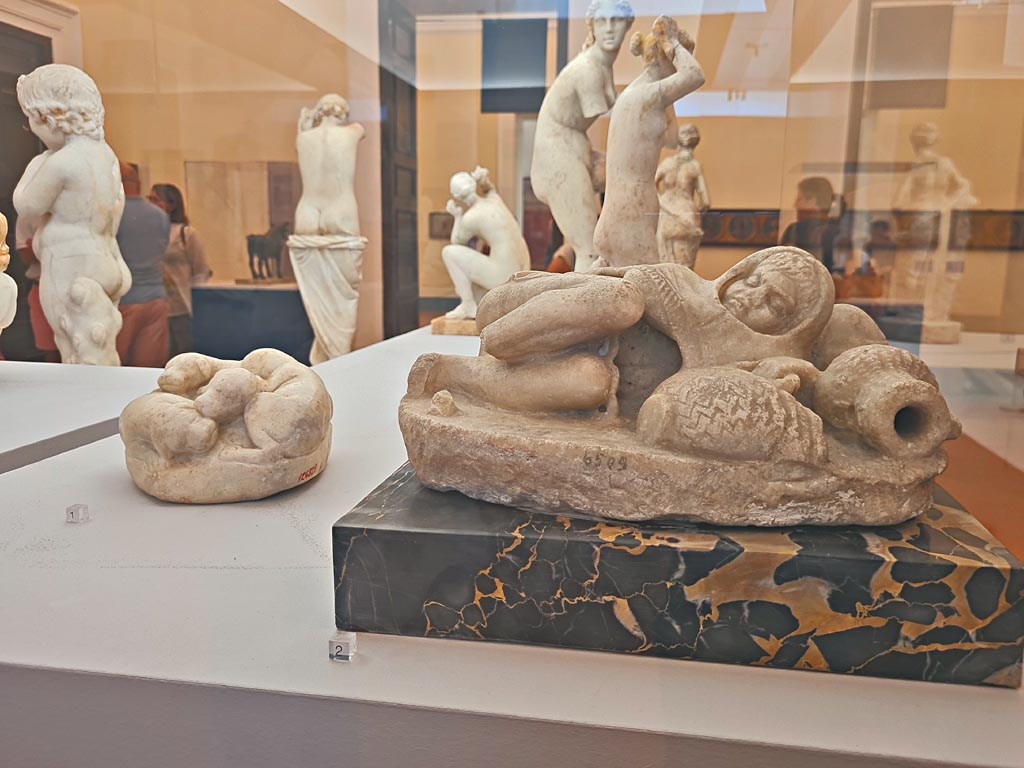 VI.12.2/5 Pompeii. October 2023. 
Marble block modelled into four puppies, on left, found near small stairs 21/5/1895, inv. 124829. Photo courtesy of Giuseppe Ciaramella. 
On the right is the marble statuette of a small sleeping fisherman found in VI.8.23, inv. 6509.
On display in “L’altra MANN” exhibition, October 2023, at Naples Archaeological Museum. 
