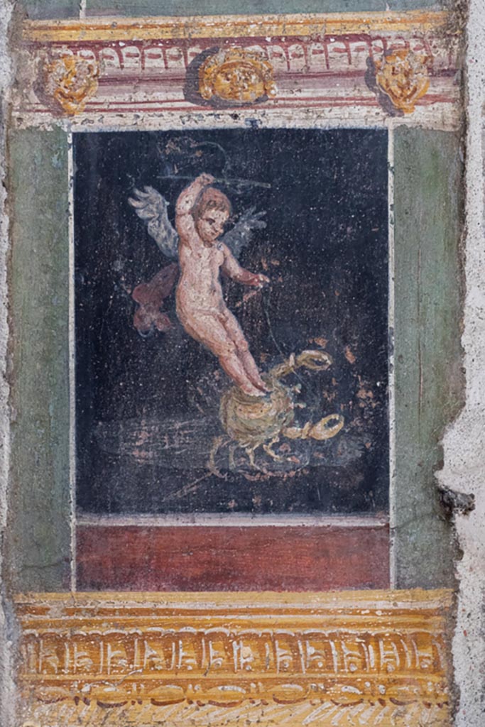 VI.15.1 Pompeii. March 2023. 
Detail of painted panel with cupid on crab on south end of west wall of atrium, leading onto peristyle. 
Photo courtesy of Johannes Eber.
