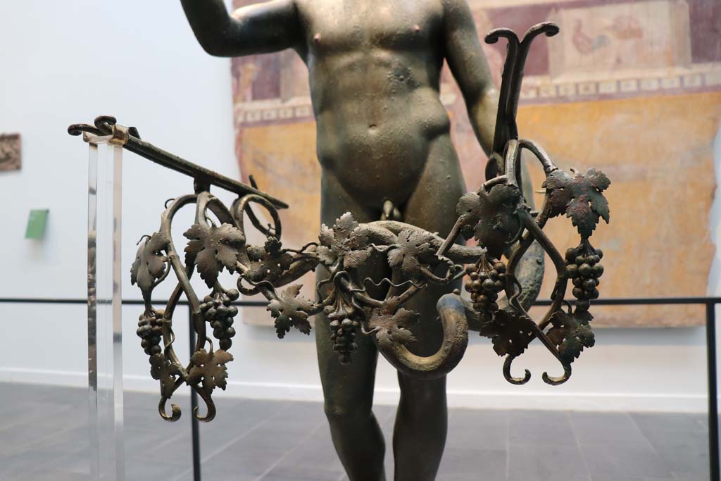 VII.16.17-22 Pompeii. February 2021. 
Detail of the addition of bunches of grapes on a vine to the statue of the bronze Ephebus, used as an oil lamp holder, found in dining room.
Photographed on display in Antiquarium. Photo courtesy of Fabien Bièvre-Perrin (CC BY-NC-SA).
