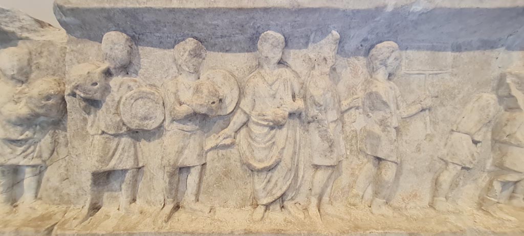SG6 Pompeii. April 2023. Detail from upper row of figures in a procession, with the deceased shown in a toga, in centre. Photo courtesy of Giuseppe Ciaramella.