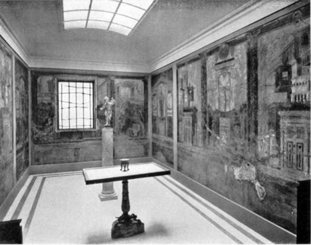 Villa of P. Fannius Synistor at Boscoreale. Cubiculum M and alcove, 1910. As displayed with frescoes and mosaic floor after the relocation of the room within the gallery. The new arrangement introduced light through the window and from a skylight in the ceiling. Note the plain mosaic floor. The table in the centre and the bronze figure Running Eros, Holding a Torch are said to be from a villa in Boscoreale. The bronze figure Running Eros, Holding a Torch is now in the Pierpoint Morgan Library in New York City. The marble table had a bronze rim decorated with a beautiful design inlaid with silver and niello. It was found in pieces and was put together with some restorations, especially in the leg. 