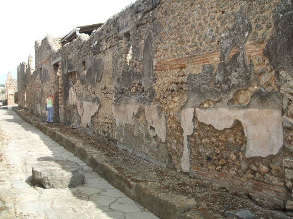 Vicolo di Tesmo looking north past remaining painted plaster on walls outside IX.7.20.
On the exterior wall of IX.7.20, opposite the doorways of IX.2.17/18, a large painted lararium was found.
According to Trendelenburg, this stood out because of the freshness and strength of the colours.
It was divided into two parts, of differing sizes. The upper part was 1.47m wide and the lower part was 4.12m wide.
The upper part showed the two Lares.
In the middle between them was the Genius with cornucopia, dressed in a white tunic holding a patera above a flaming altar. 
Behind the altar was the figure of small tibicen who played the double pipes. 
Suspended above were two garlands and above the garlands appeared the bust of Luna on the left and a bust of Sole on the right. 
The lower part showed a tall altar in the centre and three heads of Medusa. 
Two serpents approached the altar, one from each side.
See Trendelenburg in BdI 1871, pp. 199-200.
See Sogliano, A., 1879. Le pitture murali campane scoverte negli anni 1867-79. Napoli: Giannini. (p.14, No. 33).
See Frhlich, T., 1991. Lararien und Fassadenbilder in den Vesuvstdten. Mainz: von Zabern. (F65, p. 335)
