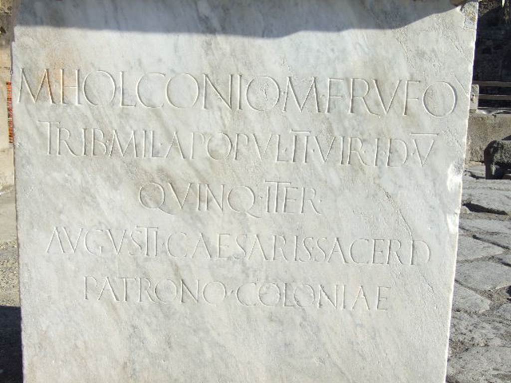 Arch of Marcus Holconius Rufus. December 2006. Latin inscription on base of statue of M. Holconius Rufus.  

M. HOLCONIO M. F. RVFO
TRIB. MIL. A POPVL. II VIR. I. D. V.
QVINQ. ITER.
AVGVSTI CAESARIS SACERD.
PATRONO COLONIAE.

According to Epigraphik-Datenbank Clauss/Slaby (See www.manfredclauss.de) this reads

M(arco) Holconio M(arci) f(ilio) Rufo
trib(uno) mil(itum) a popul(o) IIvir(o) i(ure) d(icundo) V
quinq(uennali) iter(um)
Augusti Caesaris sacerd(oti)
patrono coloniae      [CIL X 830]

According to Cooley this translates as

To Marcus Holconius Rufus, son of Marcus, 
military tribune by popular demand, duumvir with judicial power five times, 
quinquennial twice, 
priest of Augustus Caesar, 
and patron of the colony.

See Cooley, A. and M.G.L., 2004. Pompeii : A Sourcebook. London : Routledge. (Page 130, F89b). 
