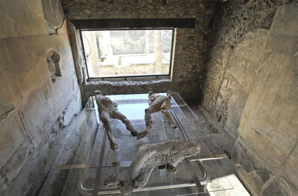 VII.1.47 Pompeii. March 2017. Room 8, looking across plaster-casts towards window in east wall.
According to the information card (shown above) –
the lower plaster-cast is a clearer photo of the woman clutching a few precious things to her bosom which she had grasped before their flight. 
She was found at the rear of the group in the Vicolo degli Scheletri. 


