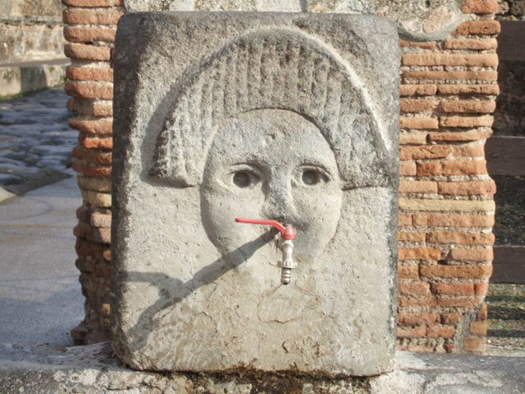 Fountain outside I.4.15 on Via Stabiana. December 2005. Relief of comedy mask.