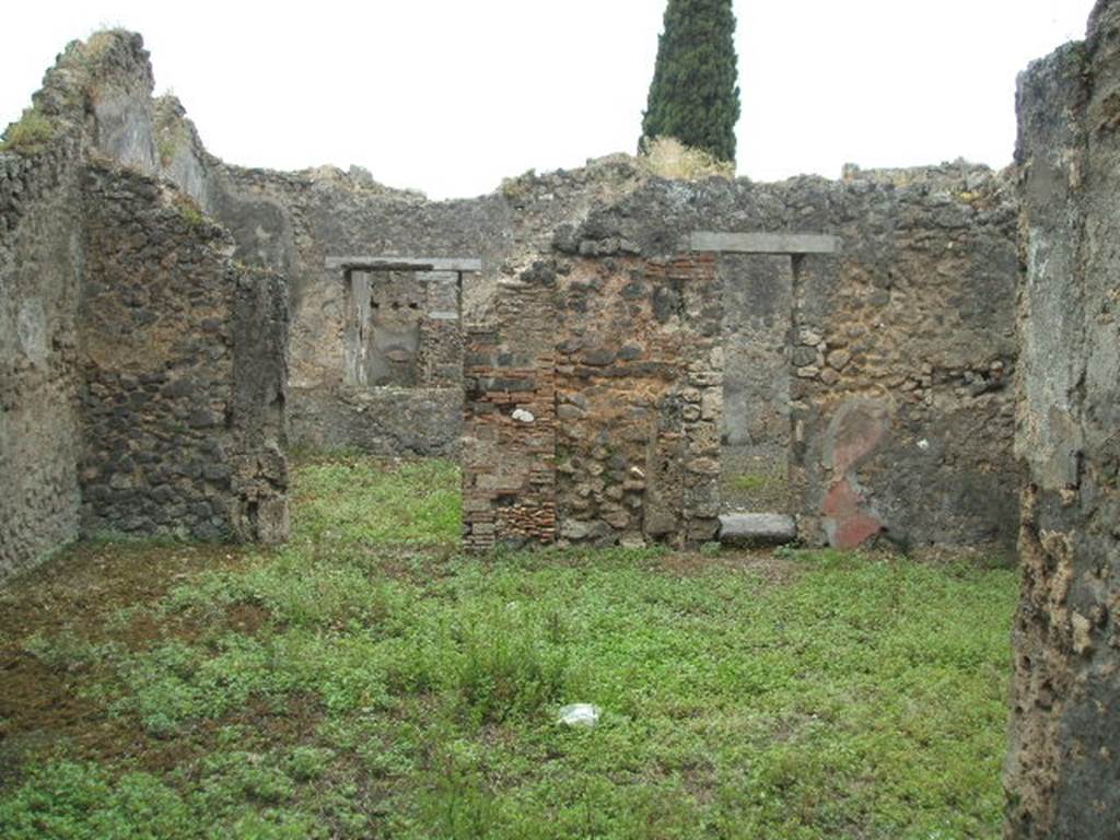 IX.9.12 Pompeii. May 2005. Looking west across room 11, the central courtyard room.
According to Boyce – on the left in the south-west corner a sacrarium was built by running a wall parallel to the south wall, and extending 1.14 from the west wall, and covering the enclosure with a sloping roof (height varies from 1.60 to 2.0). 
At the east end of this sanctuary stood a small altar of tufa (0.50 by 0.40, h.0.60) originally coated in stucco.
The inside surface of the north wall is decorated upon a white ground with a line-drawing: an aedicula and within it a male figure, standing clad in a yellow, tunic-like garment, the front of which is white between two red stripes running vertically from shoulder to hem; his flesh is reddish; in his left hand he holds a palm (?) branch at the level of his waist, in his right hand three taeniae; around his head is a fillet. The opposite south wall is also covered with white stucco, the west wall with a coarser variety.
Near the sacellum was found a female head of terracotta (h.0.17) with idealized features, 
apparently part of a statue.
He quotes reference Not. Scavi, 1889, 136, 1891, 255. 
See Boyce G. K., 1937. Corpus of the Lararia of Pompeii. Rome: MAAR 14. (p. 92-3, no.464).
