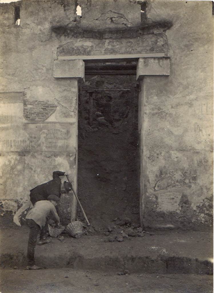 I.I.7.1 Pompeii. 6th January 1923. Entrance during excavation. Visible on each side of the doorway are the remains of electoral recommendations. Photo courtesy of Drew Baker. According to Varone and Stefani, immediately to the left of the door were a large number of electoral recommendations. To the right of the door were the electoral recommendations CIL IV 7196-8. See Varone, A. and Stefani, G., 2009. Titulorum Pictorum Pompeianorum, Rome: L’erma di Bretschneider. (p. 74

The remains of CIL IV 7212, CIL IV 7215, CIL IV 7210 (left) and CIL IV 7196 and 7197 (right) can be seen in this photograph. 

According to Epigraphik-Datenbank Clauss/Slaby (See www.manfredclauss.de) these read as:

Veientonem
aed(ilem) Primanus rog(at)       [CIL IV 7212]

L(ucium) Albucium
aed(ilem) o(ro) v(os) f(aciatis)      [CIL IV 7215]

L(ucium) Popidium Ampliatum
aed(ilem) Paquius rog(at)      [CIL IV 7210]

C(aium) Lollium Fuscum
aed(ilem) o(ro) v(os) f(aciatis)       [CIL IV 7196 ]

P(ublium) Paquium Proculum
[du]umvirum i(ure) d(icundo) vicini cupidi faciunt       [CIL IV 7197]
