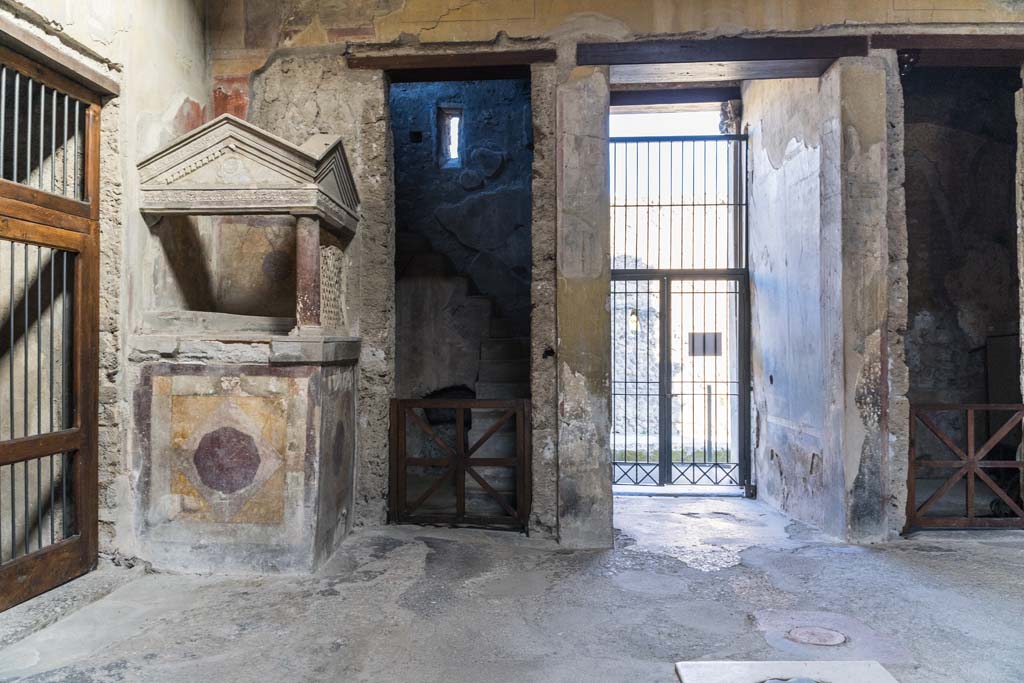 I.10.4 Pompeii. April 2022. Aedicula lararium with stucco decoration, in north-west corner of atrium. 
Behind is room 2 with stone stairs to an upper floor. Photo courtesy of Johannes Eber.
