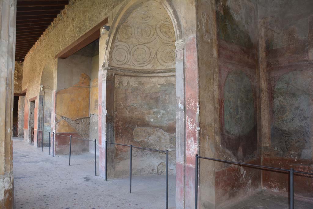 I.10.4 Pompeii. September 2019. Looking towards south side of south portico, from south-west corner.
On the right is Alcove 25 (Sacrarium), followed by Alcove 24, 23, and 22 and doorway to 21, in south-east corner.
Alcove 24 has a domed top decorated with stucco, underneath which is a painting of Venus and cherubs in a temple.
Alcove 23 has the painting of the seated poet Menander. 
Alcove 22 also has a domed top decorated with stucco, underneath which is a painting of Diana and Acteon.
Room 21 has a mosaic emblema of satyr and maenad in the centre of the mosaic floor.
Foto Annette Haug, ERC Grant 681269 DÉCOR.

