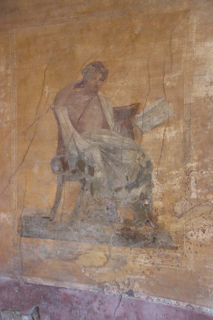 I.10.4 Pompeii. September 2021. 
Alcove 23, west wall with wall painting of a seated poet. Photo courtesy of Klaus Heese.
The name of Menander was inscribed by the painter on the skirt of the man’s cloak. 
In this alcove there are also painted masks, with possibly Bacchus sitting on a chair with a robe covering his legs, and a painted table.

