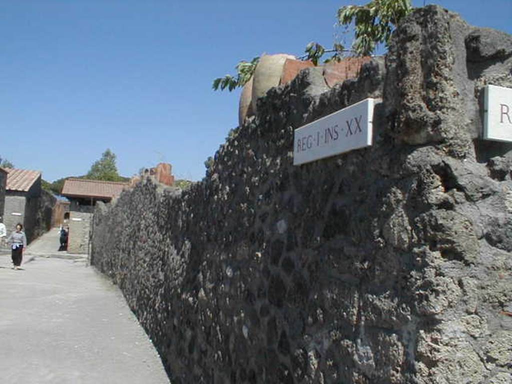 Via della Palestra, looking east along exterior north wall of I.20.5. May 2005.
According to Jashemski, the broken amphorae inserted in the top of this wall would have protected the garden from thieves.
The large phallus carved in Sarno limestone, painted red, and inserted on the west end of the outside of the north wall gave protection from evil. 
See Jashemski, W. F., 1993. The Gardens of Pompeii, Volume II: Appendices. New York: Caratzas. (p. 67).

