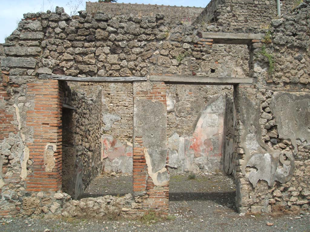 V.2.g Pompeii. May 2005. Room ‘k’ on the east of the atrium, with remains of painted plaster.
According to NdS, this room which had a window onto the atrium, was decorated with opus signinum flooring.
The walls were divided into red and white panels with a white frieze, and black dado.
In the central white panel of each wall was a painting.
When excavated, only the one on the east wall remained, and the lower edge of the one on the south wall. 
According to Sogliano, from what he could see and described from the painting on the south wall, he thought it had probably been a representation of Perseus freeing Andromeda.
In each of the panels was a flying figure, painted on a red background. 
Also seen on the south wall on the red plaster was a graffito of the following numerals:
XXIIIII
XXIIIII
XXXI
See Notizie degli Scavi di Antichità, 1896, (p.420)
