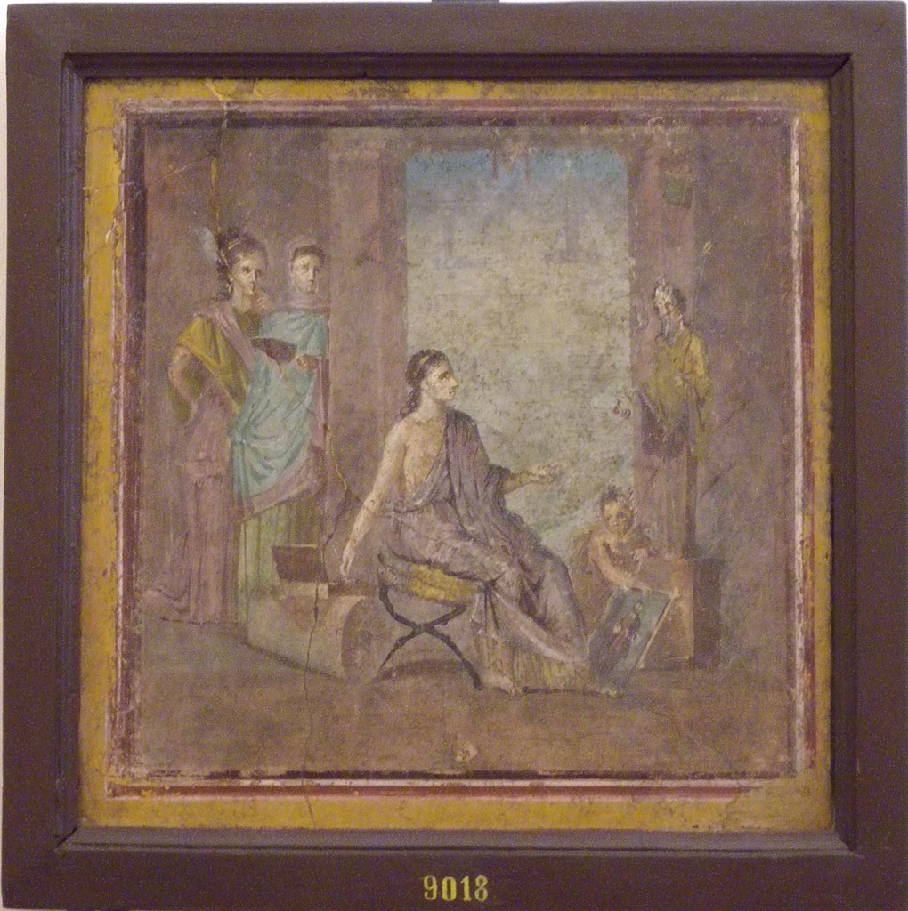 VI.1.10 Pompeii. December 2007. Found 22nd June 1771 on east wall of room 9, room to south of garden.  
Wall painting of a young woman painting a herm of Dionysus.
A cupid is holding the unfinished picture while she mixes colours on her palette. 
Two other maidens are watching the artist with unfeigned interest.
See Mau, A., 1907, translated by Kelsey F. W. Pompeii: Its Life and Art. New York: Macmillan.  (pp. 280-2, T. 133).
Now in Naples Archaeological Museum. Inventory number 9018.
