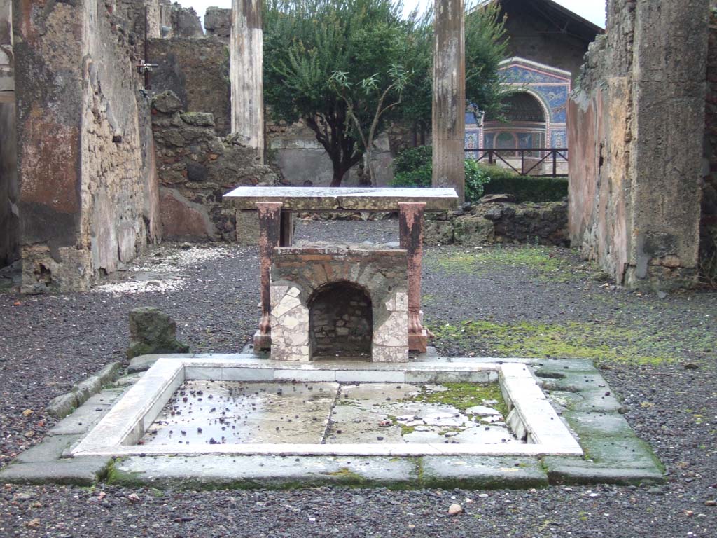 VI.14.43 Pompeii. December 2007.  Room 1, impluvium in atrium, marble table and marble covered brick base or fountain. According to Jashemski, unique so far at Pompeii, is the tiny mosaic fountain (about 0.50m high) in the atrium. It had been built on the east edge of the impluvium, facing the entrance during the last years of the city. 
According to Sear, the front and bottom of the inside walls were lined with marble.  Above this there was a “line of shells and then a zone of mosaic, in white, yellow, and blue, and above the mosaic another line of shells”.   The head of the niche was covered with pumice and marine deposits. See Jashemski, W. F., 1993. The Gardens of Pompeii, Volume II: Appendices. New York: Caratzas. (p.152)

