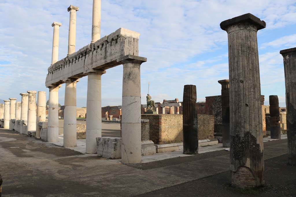 VII.8 Pompeii Forum. December 2018. Looking north-east from south-west corner. Photo courtesy of Aude Durand.
On the west side, centre left, the columns of the Forum were replaced. On the south side, on the right, the original columns of the portico still remains.
“The ancient portico of the Forum of Pompeii, of tufa covered with stucco, of Greek (Doric) style, in later times was largely replaced, or it probably all had to be, by a portico in that limestone, called travertine in Naples, of heavier and less beautiful form, but of more solid and perfect construction. 
On the entire west side, the ancient portico was demolished – still recognizable by the bases remaining in place – and they built or began to build the new one. On the south side, and on that part of the east side that is south of the road called Via dell'Abbondanza, the ancient portico remained.” 
(L’antico portico del Foro di Pompei, di tufo rivestito di stucco, di stile greco (dorico), in epoca posteriore fu in gran parte rimpiazzato, o doveva esserlo probabilmente tutto, da un portico in quella pietra calcare che a Napoli si chiama travertino di forme più pesanti e poco belle, ma di costruzione più solida e perfetta. Sul intera lato ovest fu demolito l’antico portico – riconoscibile ancora dalle basi rimaste al posto – e costruito, o cominciato a costruire quello nuovo. Sul lato sud, e su quello parte del lato est che sta a sud della strada detta – dell’Abbondanza, rimase il portico antico.)
See Mau, in Bullettino dell’Instituto di Corrispondenza Archeologica (DAIR), 06, 1891, (p.168).
