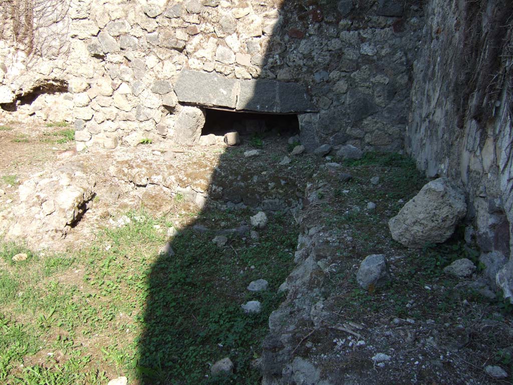 VII.12.7 Pompeii. September 2005. Looking east to remains of oven and workbench near south wall.
According to Boyce, on the south wall of the room with the oven was a large lararium painting.
In the centre was a blazing tripod, with the Genius to the right of it.
On each side was a wreathed Lar. 
To the left of this group stood Vesta, at her side was an ass with a bell around its neck.
On the right of the group stood Mercury.
In the lower zone, marked off from the upper by a brownish stripe, were the two serpents.
They were approaching a gold-coloured altar, on top of which was a white shallow dish containing a blazing fire.
In the fire was an egg and several fruits – a date, a pomegranate and a medlar.
See Boyce G. K., 1937. Corpus of the Lararia of Pompeii. Rome: MAAR 14. (p.70, no.313) 
See Helbig, W., 1868. Wandgemälde der vom Vesuv verschütteten Städte Campaniens. Leipzig: Breitkopf und Härtel. (68)
According to BdI, this was the first time that Mercury appeared associated with the Lares, in Pompeii.
See Bullettino dell’Instituto di Corrispondenza Archeologica (DAIR), 1864, p.114-115 (described as Casa II.)
