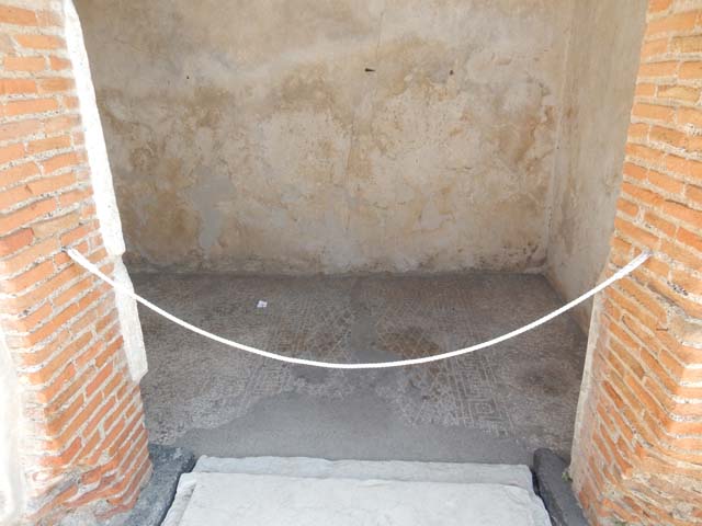 VIII.2.16 Pompeii. May 2017.  Threshold to doorway of cubiculum in centre of south wall of atrium. Photo courtesy of Buzz Ferebee.
The indents in the limestone threshold clearly show that the doorway was fitted with wooden door-jambs and that its doors opened inside the room, where the floor decoration clearly defined the anticamera and the bed alcove. The floor is seen with a “carpet” outline of white tesserae in a diamond shaped net design with a border of meanders alternating with squares and a central tessera.

