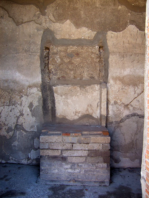VIII.2.16 Pompeii. September 2005. Remains of aedicula household shrine.
According to Boyce, in the third small room on the south of the atrium, against he south wall stand the ruins of an aedicula.
A masonry podium that was ornamented along the upper edge with a stucco cornice, supported the shrine.
The shrine was built of tufa and coated with white stucco contemporary with the walls of the room.
This was spread not long before the catastrophe.
The inside of the aedicula was divided into two storeys, each supported by two columns and two antae.
The roof was flat and adorned with terracotta antefixes.
One of these was preserved and represented a male face in the centre of a kind of palmette.
Nearby was found a small tufa altar,
See Notizie degli Scavi di Antichità, 1893, 48. 
See Boyce G. K., 1937. Corpus of the Lararia of Pompeii. Rome: MAAR 14. (p.74, no.343) 
