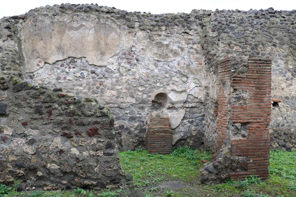 VIII.4.12, Pompeii. December 2018. Looking west into kitchen, room on west of side of tablinum. Photo courtesy of Aude Durand.
According to Boyce, the room on the right of the tablinum may have been the kitchen.
He says in the west wall, pictured above, there was an arched niche.
Its walls were coated with white stucco which was painted with red and yellow flowers.
On the right side of the niche, the lararium painting was painted in two zones.
The lower zone showed a serpent, still visible in 1937, with a red crest and beard, rearing its head above the masonry altar.
The altar was standing against the wall below the niche.
In the upper zone, nothing was visible, but earlier reports described the figure of a Lar painted on the left side of the niche.
On the right side of the niche, there were two painted hams and an eel.
See Boyce G. K., 1937. Corpus of the Lararia of Pompeii. Rome: MAAR 14. (p.76). 
See Pappalardo, U., 2001. La Descrizione di Pompei per Giuseppe Fiorelli (1875). Napoli: Massa Editore. (p.128).
