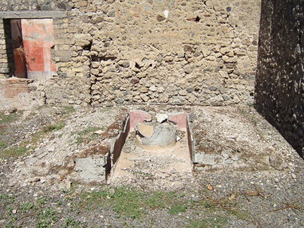 VIII.5.39 Pompeii. September 2005. Summer triclinium.  
According to Soprano –
Ubicazione: giardino. L. medius, m.2.63; l. imus, m.3.45; l. summus, m.310; diametro della mensa, m.0.59.
Bibliog. “Bull.Inst“, 1889, p.128; Mau, op. c. p.336; Mau-Kelsey, p. 333.
Su un battuto di cocciopesto, in un angolo del viridario, era situato il triclinio con i tre letti a piano inclinato, con tracce di cocciopesto colorato in giallo. 
Le pareti verticali, invece, rivestite d’intonaco rosso, erano originariamente decorate con pitture oggi quasi totalmente svanite.
Il l. imus era piu lungo, del l. summus. 
La mensa, circolare, rivestita di intonaco grezzo, presenta nel piano un rivestimento di segmenti di marmo di vario colore e dimesione. 
Il foro al centro di esso serviva al passaggio di un fistula per getto d’acqua.”
See Soprano, P. (1950). I triclini all’aperto di Pompei. (In Pompeiana, raccolta di studi per il secondo centenario degli scavi di Pompei. Napoli, Gaetano Macchiaroli, Editore, P. 301, no.16).
