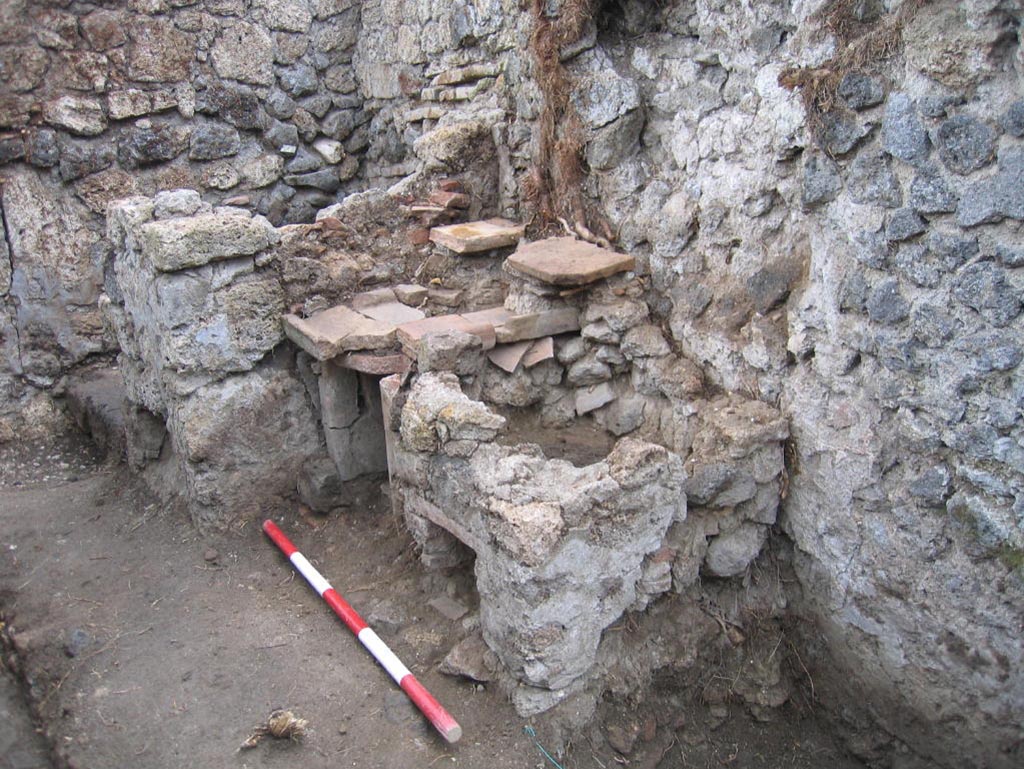 VIII.7.10 Pompeii. August 2005. Looking south-east in kitchen area towards hearth at east end of south wall.
The remains of the lararium niche may be partly visible on the upper right of centre of the photo.
Photo courtesy of Pompeii Archaeological Research Project: Porta Stabia.
According to Mau -
“Next to the hearth there was the usual painting of the Lares, and a niche.”
See Mau in BdI, 1875, (p.167) (p.166-169 below_- La quarta casa). 
