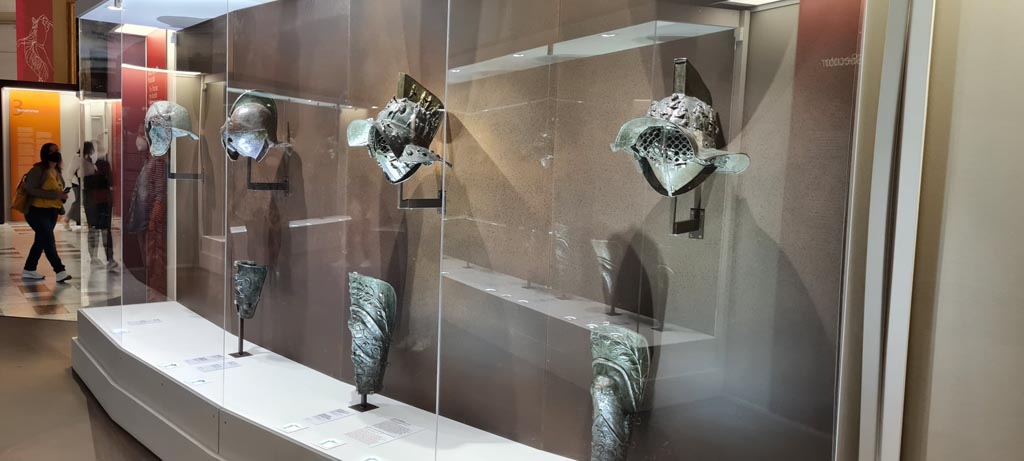 Display cabinet with helmets and greaves in Naples Archaeological Museum. May 2021. Photo courtesy of Giuseppe Ciaramella.