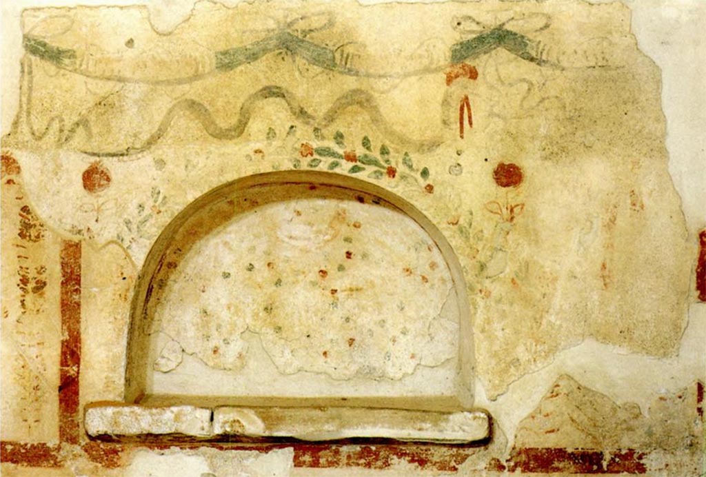 Scafati. Villa rustica in proprietà Rosa Buccino via Tenente Jorio. Small lararium in the form of a semicircular niche.
At the top is a garland of ribbons. Above the top of the niche is a serpent moving to the right.
Around the rim of the niche is border of a plant with red flowers and a larger red flower is on each side at the top. 
The interior of the niche has a red and green pattern on a white background.
To the right are what may be the legs of a figure.
See Conticello de' Spagnolis, M., 1994. Il Pons Sarni di Scafati e la via Nuceria-Pompeios, Soprintendenza Archeologica di Pompei Monografie, 08, p. 31, fig. 19.


