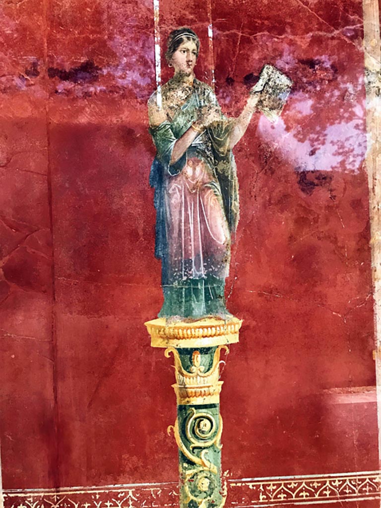 Complesso dei triclini in località Moregine a Pompei. April 2019. Triclinium A, north wall, Apollo with cithara. 
Photo courtesy of Rick Bauer.
This has also been suggested as Erato, the Muse of lyric poetry, particularly erotic poetry, and mimic imitation, who is often depicted with a wreath of myrtle and roses, and holding a lyre, or a small kithara, a musical instrument often associated with Apollo.

