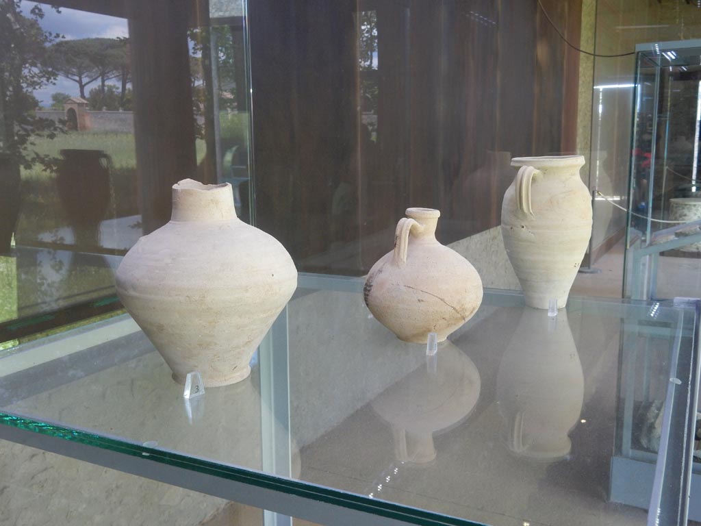 Complesso dei triclini in località Moregine a Pompei. May 2018. Finds on display in Pompeii Palaestra.
Blown glass perfume vessel.
Blown glass drinking cup with drops decoration.
Common ware lids of local production.
Red terra sigillata base from a plate of central-italic origin with the maker mark L(ucius) R(asinius) P(isanus).
Two fritilli used for dice throwing.
Photo courtesy of Buzz Ferebee.

