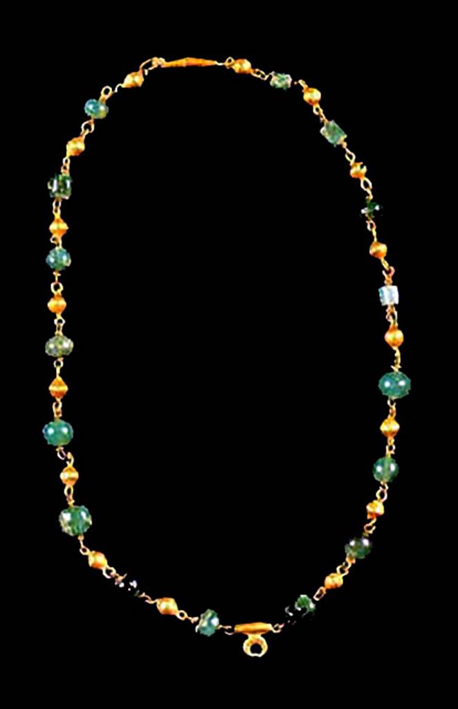 Oplontis, Villa of Lucius Crassius Tertius. Necklace found in room 10, in 1984, under the head of skeleton no. 14.
It comprised of 16 green stones alternated with 18 small spheres with gold foil. 
It has a pendant of a small crescent moon.
See D’Ambrosio A., 1987. Rivista di Studi Pompeiana I, p. 176, fig. 45.
Oplontis inventory number 3307.
See D’Ambrosio, A., 2001. Women and Beauty in Pompeii. Roma: Bretschneider, p. 56, fig. 20.

 
