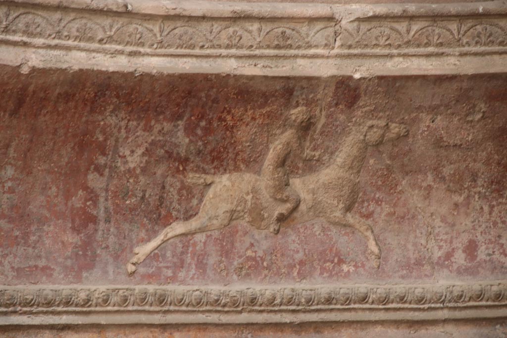 VII.5.24 Pompeii. October 2023. Frigidarium, detail of plasterwork showing a cupid on horseback. Photo courtesy of Klaus Heese.