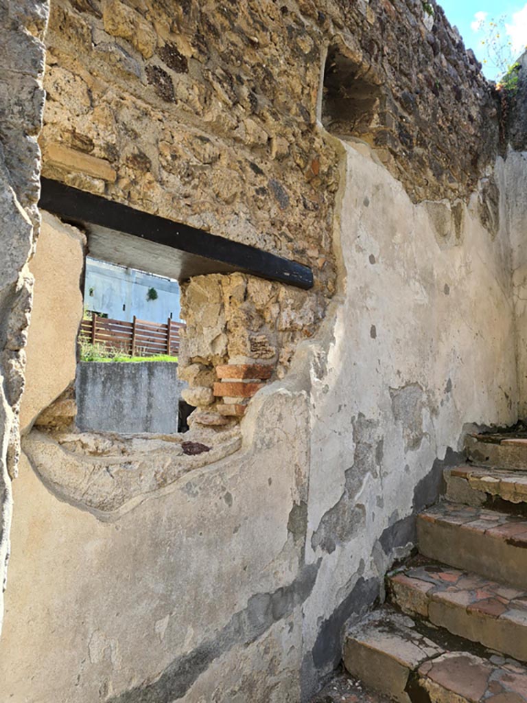 HGW24, Villa of Diomedes, Pompeii. May 2024. 
East wall at side of stairs, with lararium niche in upper wall with window below. Photo courtesy of Klaus Heese.
According to Boyce,
Just to the right of the main entrance six steps lead down to the servants’ quarters, and in the wall beside this stair is a piccolo larario – apparently only a niche, in which a statuette of Minerva was found.
See Boyce G. K., 1937. Corpus of the Lararia of Pompeii. Rome: MAAR 14, (p.97, no.476).
See Giacobello, F., 2008. Larari Pompeiani: Iconografia e culto dei Lari in ambito domestico. Milano: LED Edizioni, (p.221, no.3).

