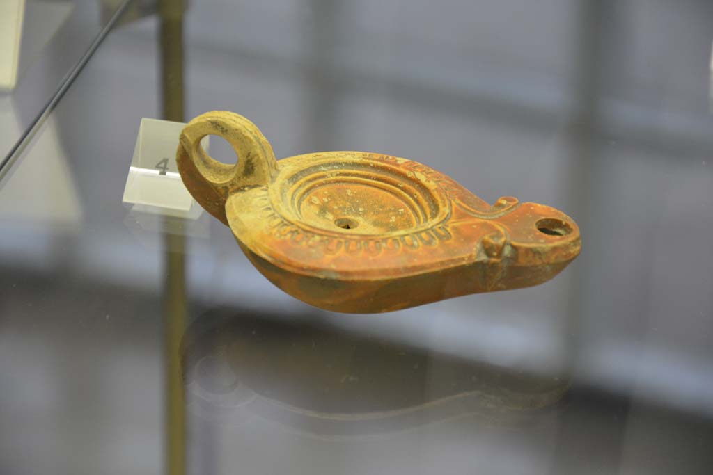 Villa Regina, Boscoreale. April 2017. Above, no.4, terracotta one-handled single flame lamp. Photo courtesy of Adrian Hielscher.
Villa Regina, Boscoreale, (from information card) –
The terracotta lamps found in the villa are of a one handled type, with a beak from which the flame shone. On the bronze support would have leaned the lamp. 
A lamp, which bears a cross sign on the external base, documents the human presence in the area of the villa after the eruption of 79AD.

Le Lucerne fittili rinvenuti nella villa sono di tipo monolicne, ad un becco da cui fuoriusciva la fiamma. Sul sostegno di bronzo veniva poggiata la lucerna.
Una lucerna, che reca sul fondo esterno un segno a croce, documenta la presenza umana nell’area della villa dopo l’eruzione del 79AD.

No.3 (not photographed). A bronze support for a lamp, found in room 2, dateable from Ist century AD.
Nos. 4-6. One-handled lamps, made of terracotta, dateable from 1st century AD.
No.7 (not photographed). A one-handled lamp, made of terracotta, dateable from II to IV century AD.

